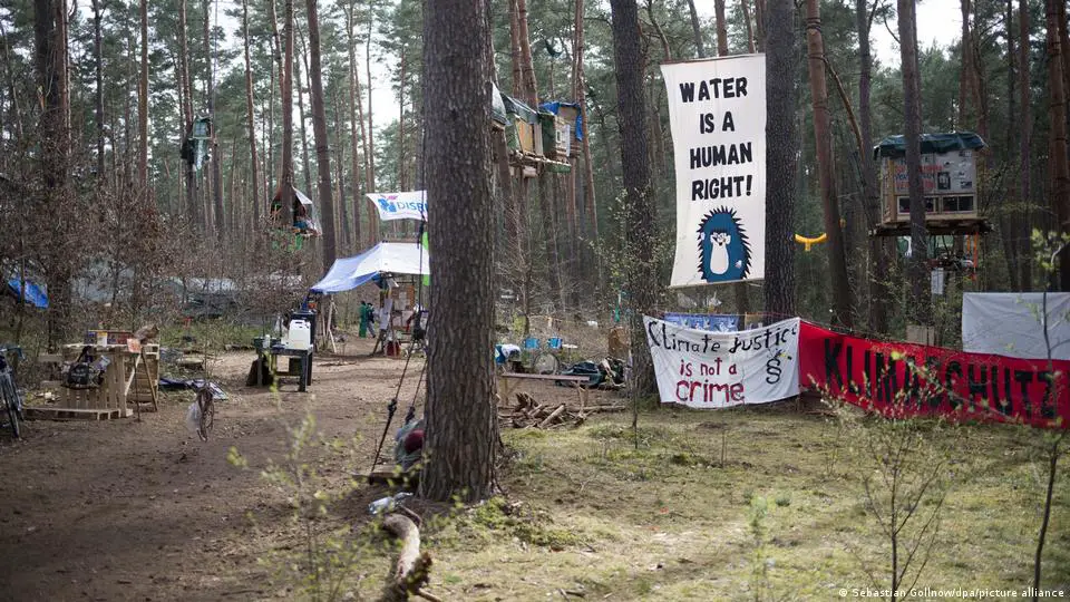Ein Protestcamp mit Schildern mit der Aufschrift „Wasser ist ein Menschenrecht“ und „Klimagerechtigkeit ist kein Verbrechen“ in einem Wald in Grünheide, Deutschland
